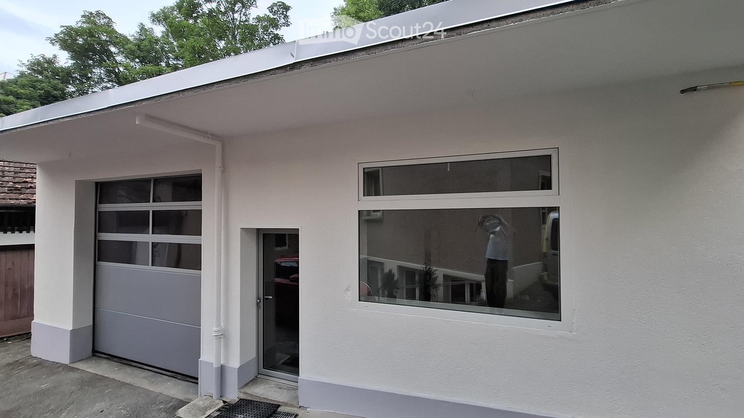 Single-story building with a garage, white exterior, large windows, and a flat roof.