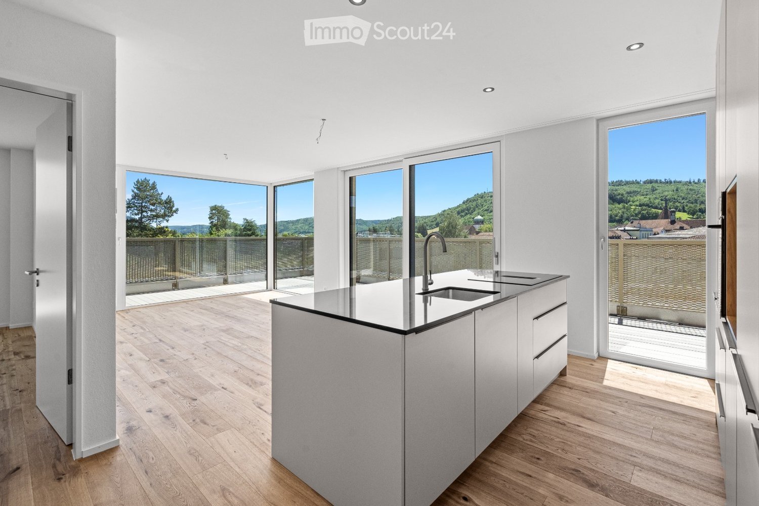 Modern kitchen with light-colored cabinets, a central island, and large windows offering a scenic view of the landscape.