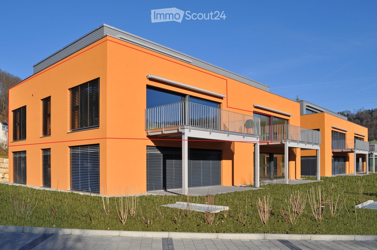 Modern two-story building with orange facade, large windows, balconies, and a garage entrance.