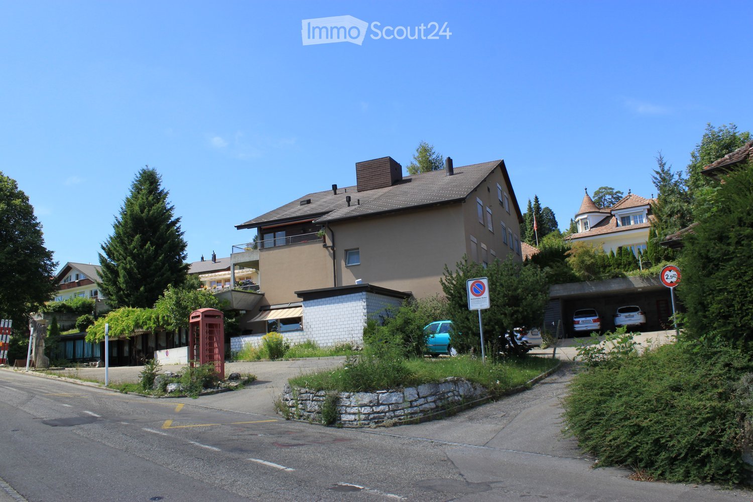 A two-story residential building with a balcony, garage, and surrounding greenery.