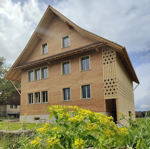 Two-story house with a brown facade, multiple windows, and a decorative wooden lattice on one side.