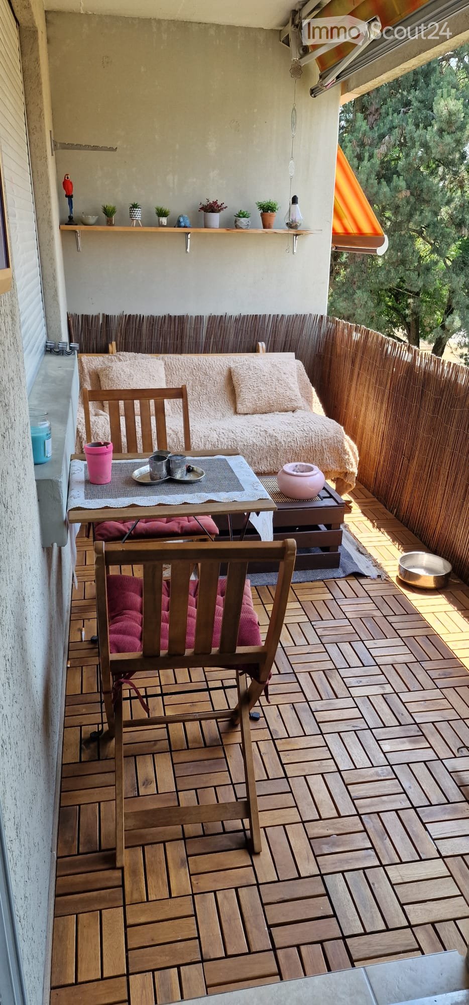 Balcony with wooden decking, sofa, small table, chairs, and potted plants.