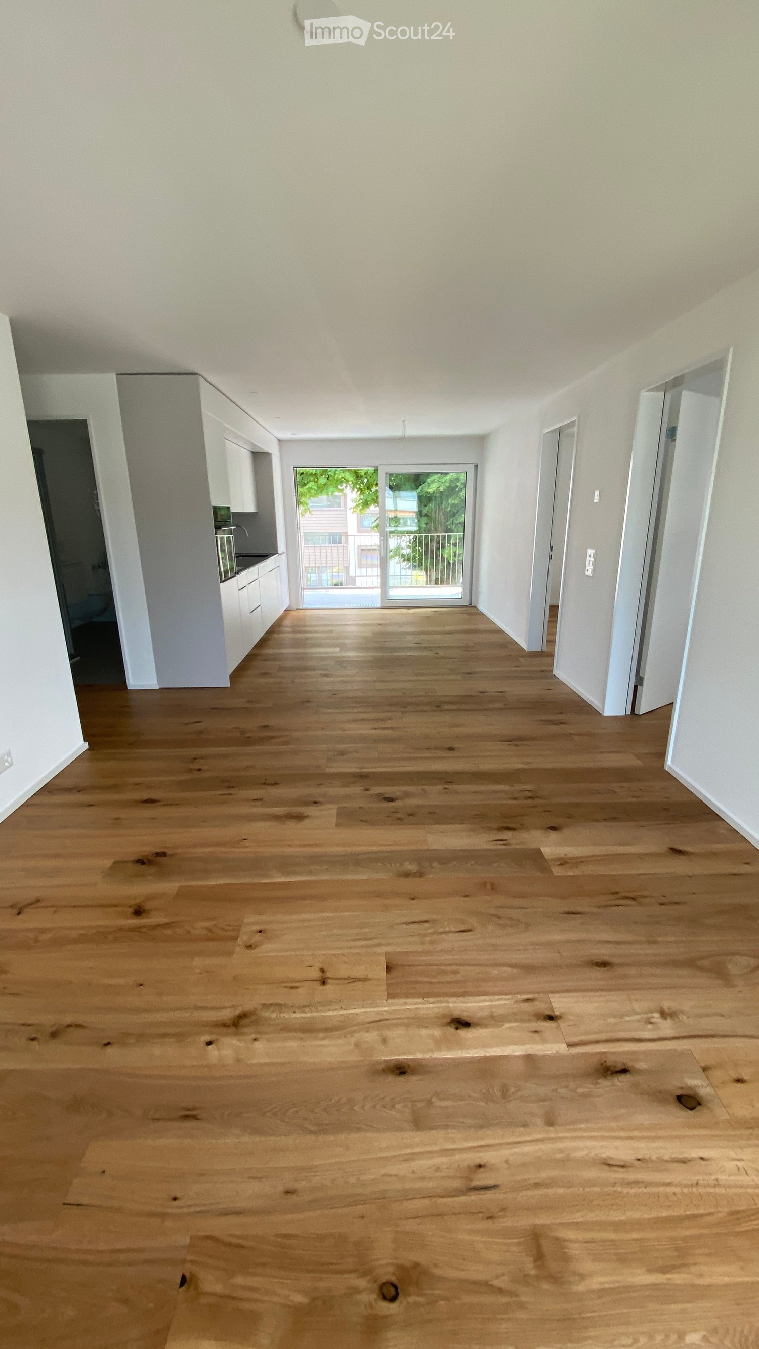 Empty room with light wooden flooring, white walls, and a sliding glass door leading to a balcony.