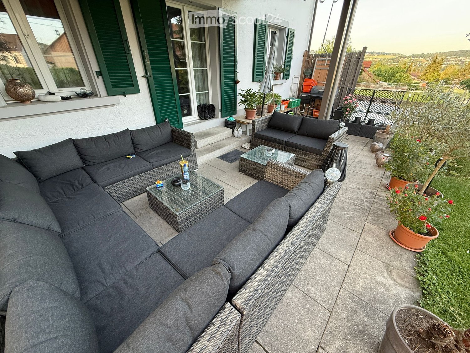 A spacious outdoor patio with a grey sectional sofa, glass coffee tables, wicker chairs, and potted plants.