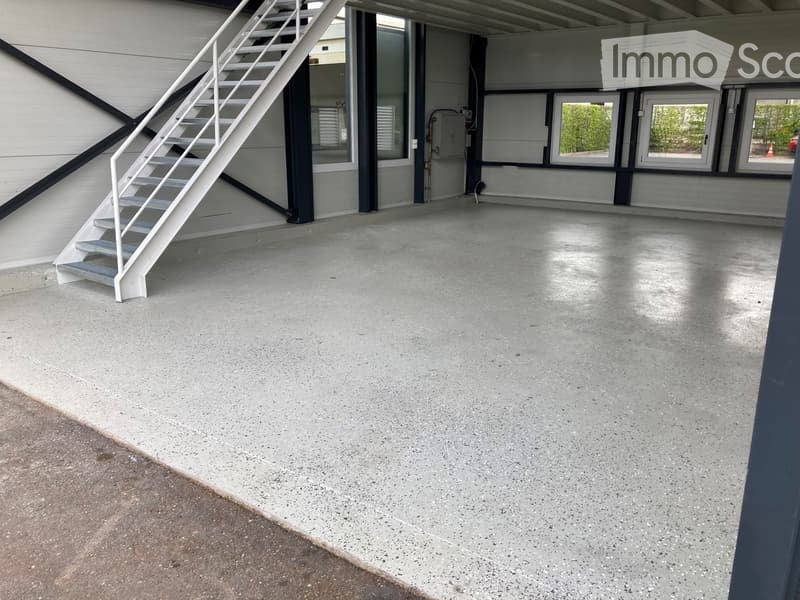 Empty garage with concrete floor, white metal staircase leading up, large windows, and industrial-style doors.