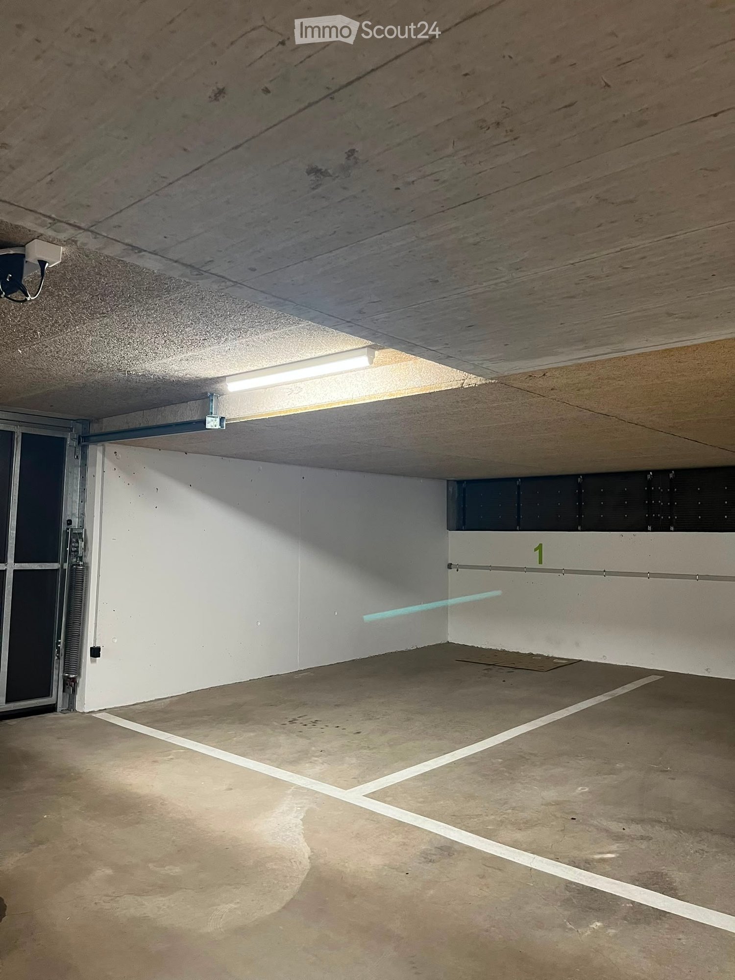 Empty underground parking space with concrete floor, white walls, fluorescent lighting, and marked parking spaces.