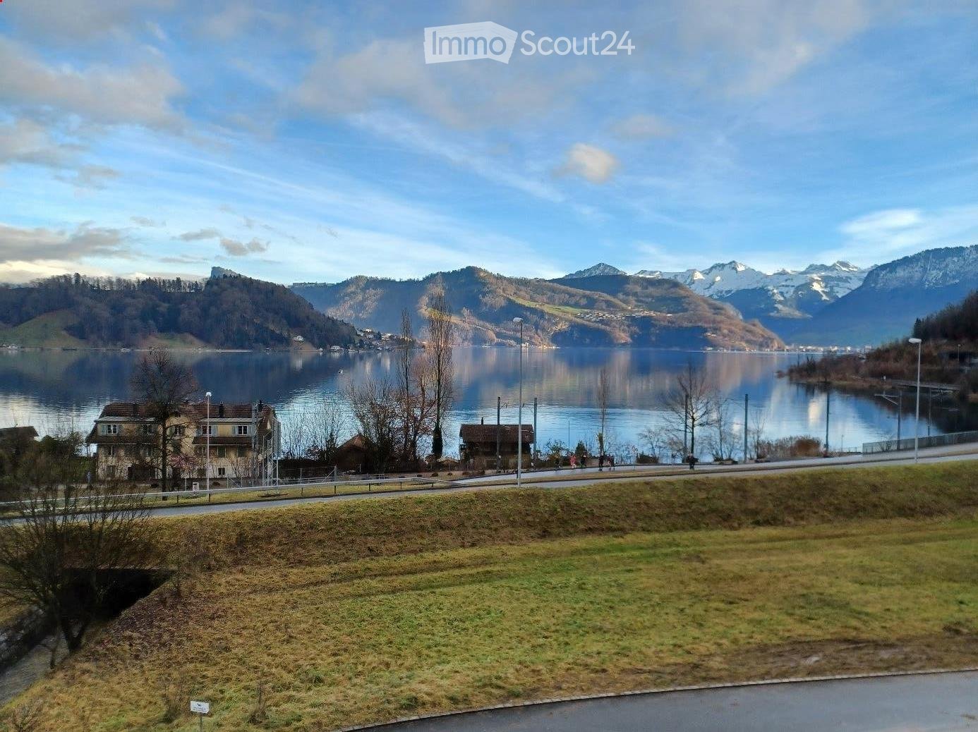 Scenic lakeside view with calm water, distant mountains, and a few houses along the shore.