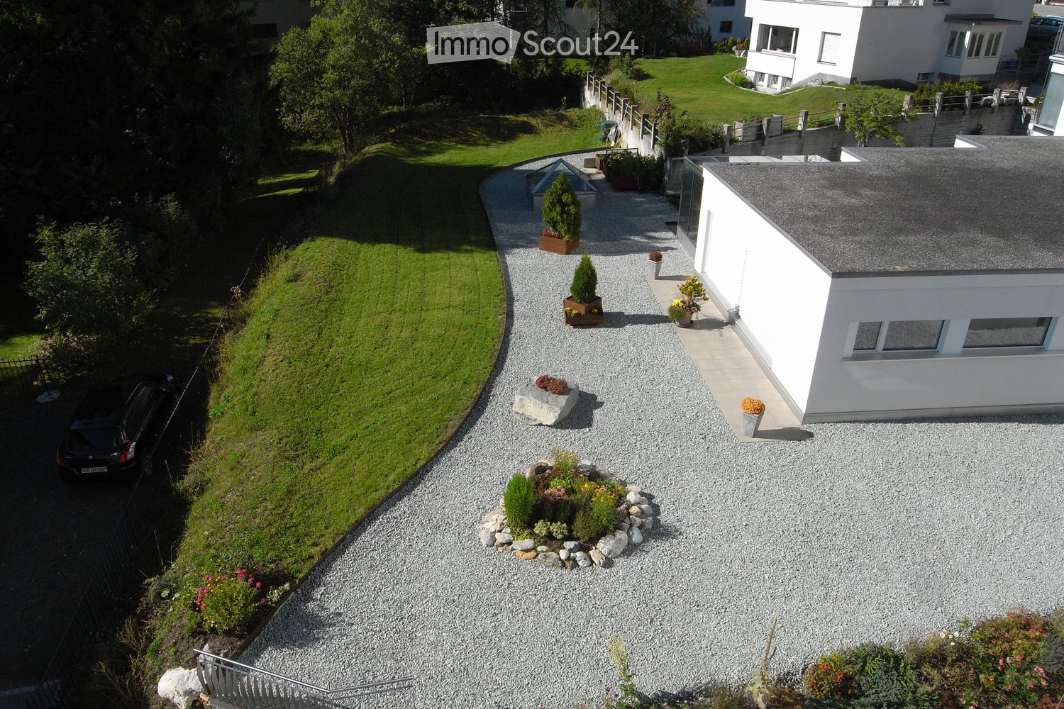 Aerial view of a modern house with a well-maintained garden, gravel driveway, and landscaped greenery.