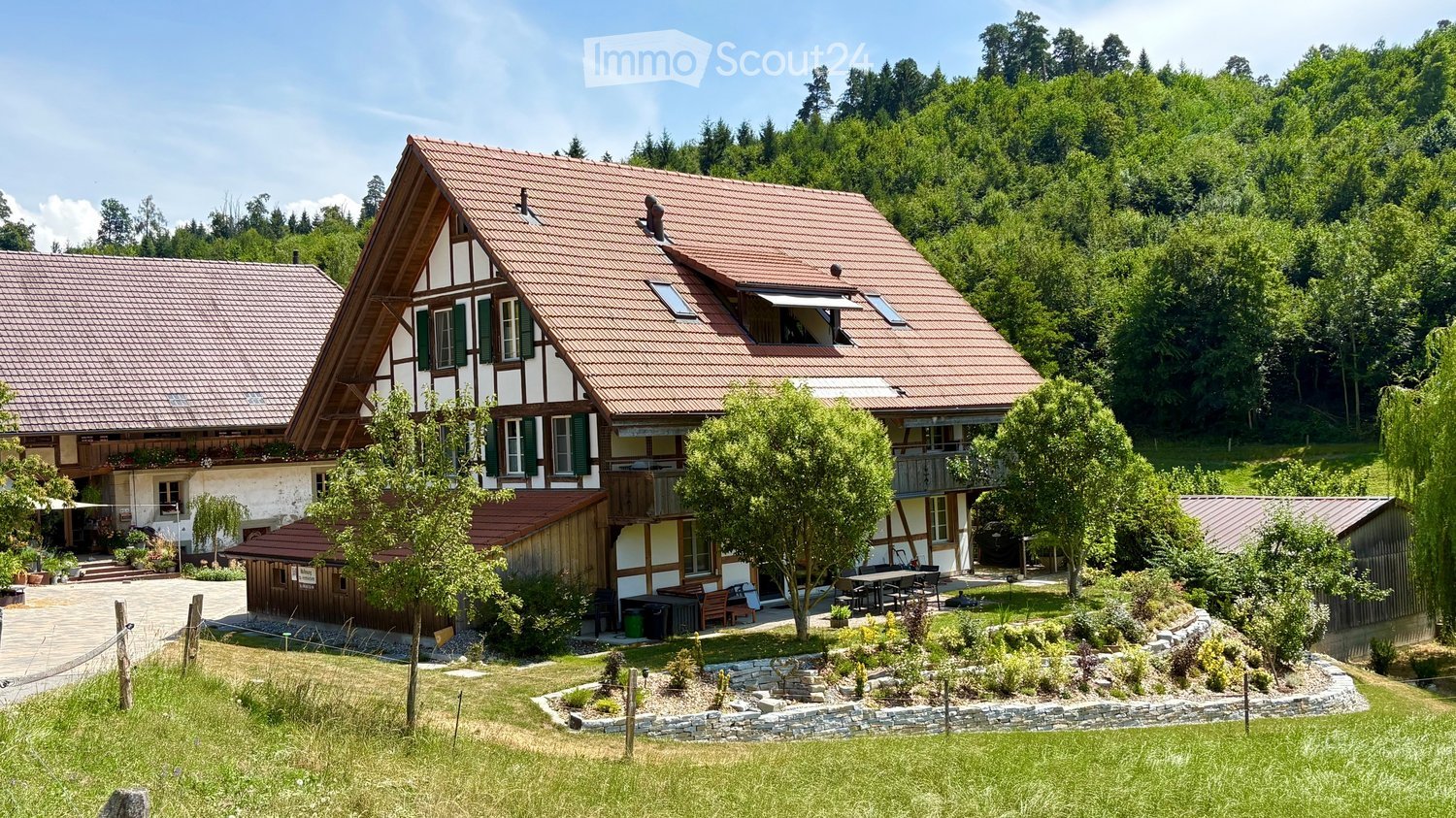 A two-story house with a red-tiled roof, white and brown exterior, surrounded by a well-maintained garden and trees.
