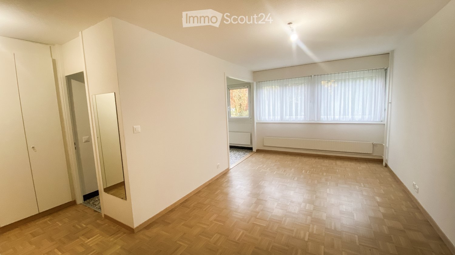 Empty room with wooden flooring, white walls, and large windows with blinds. No furniture or equipment present.