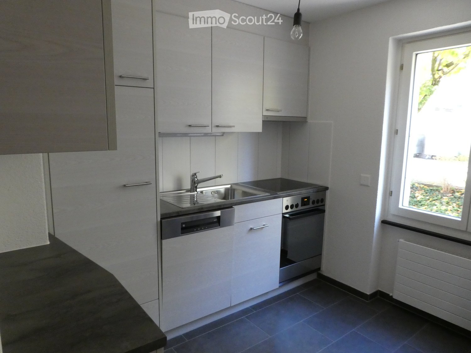 Modern kitchen with white cabinets, stainless steel sink, oven, and dishwasher. Features a window with a view of greenery outside.