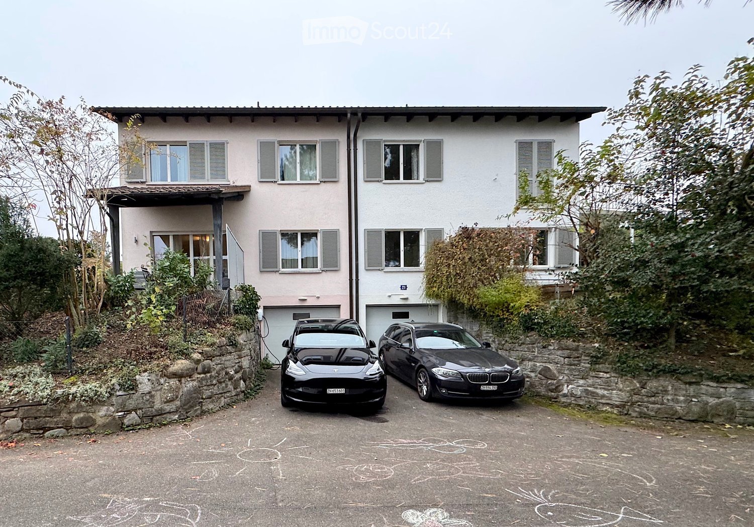 Two-story house with light pink and white exterior, multiple windows with shutters, garage, and two parked cars in front.