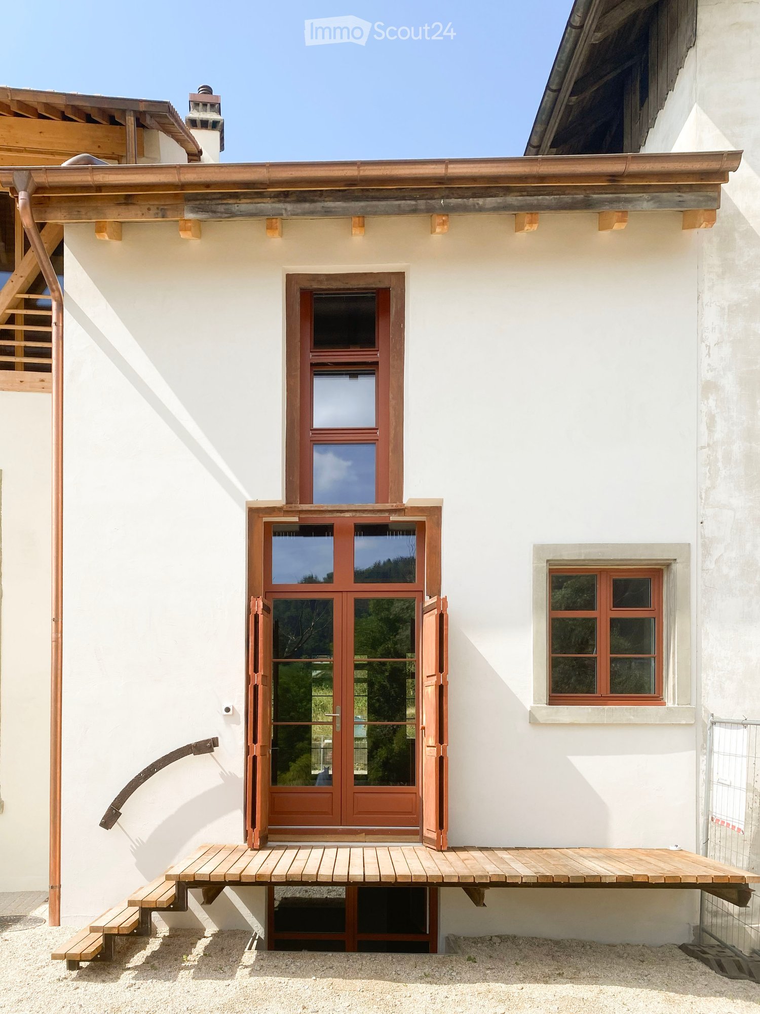 A two-story house with white walls, wooden doors, and a raised wooden platform leading to the entrance.