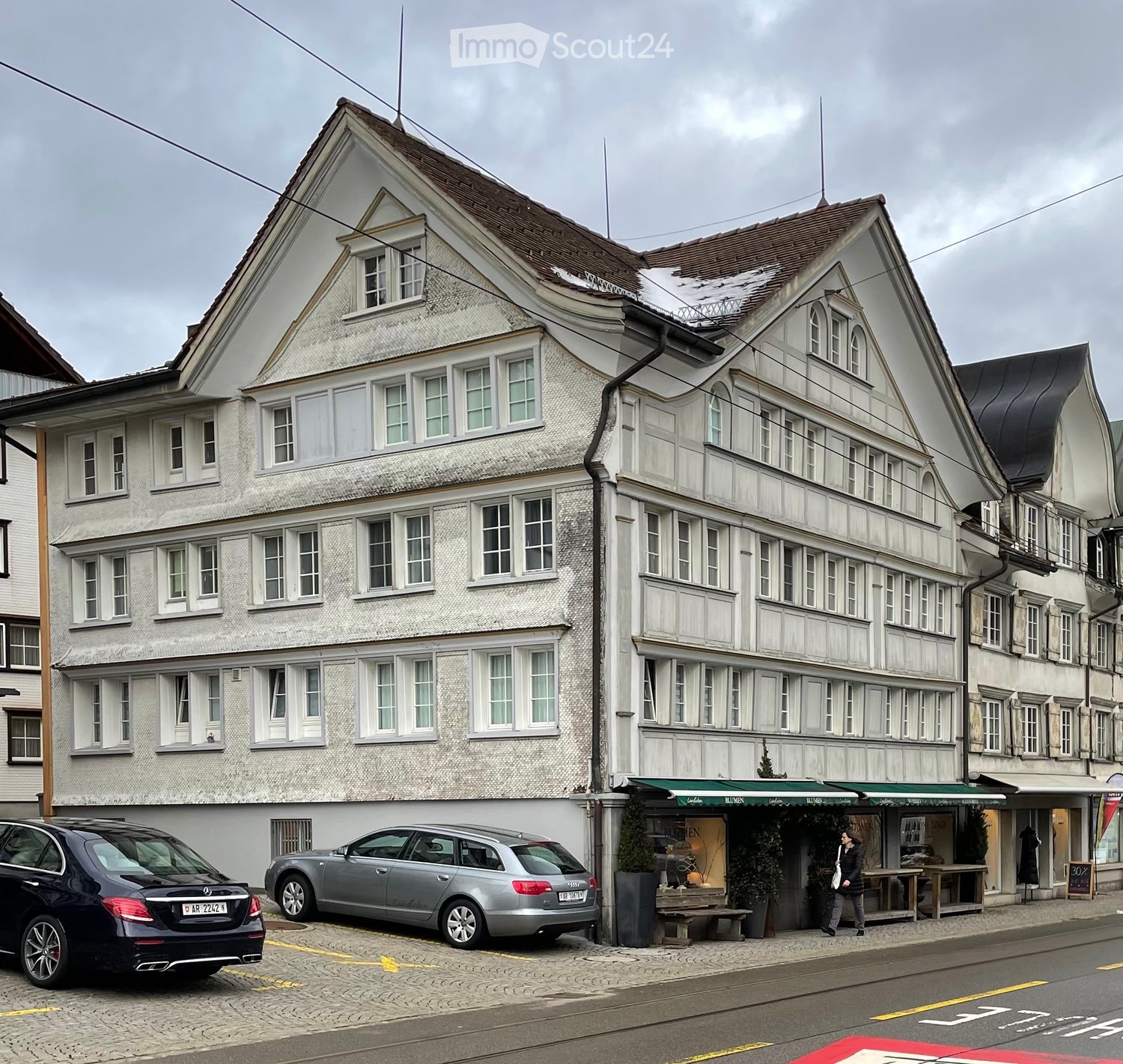3 story building, white exterior, multiple windows, brown roof, cars parked in front
