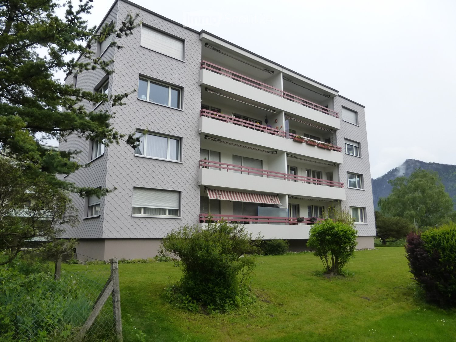 Modern multi-story apartment building with balconies, large windows, and a well-maintained lawn in front.