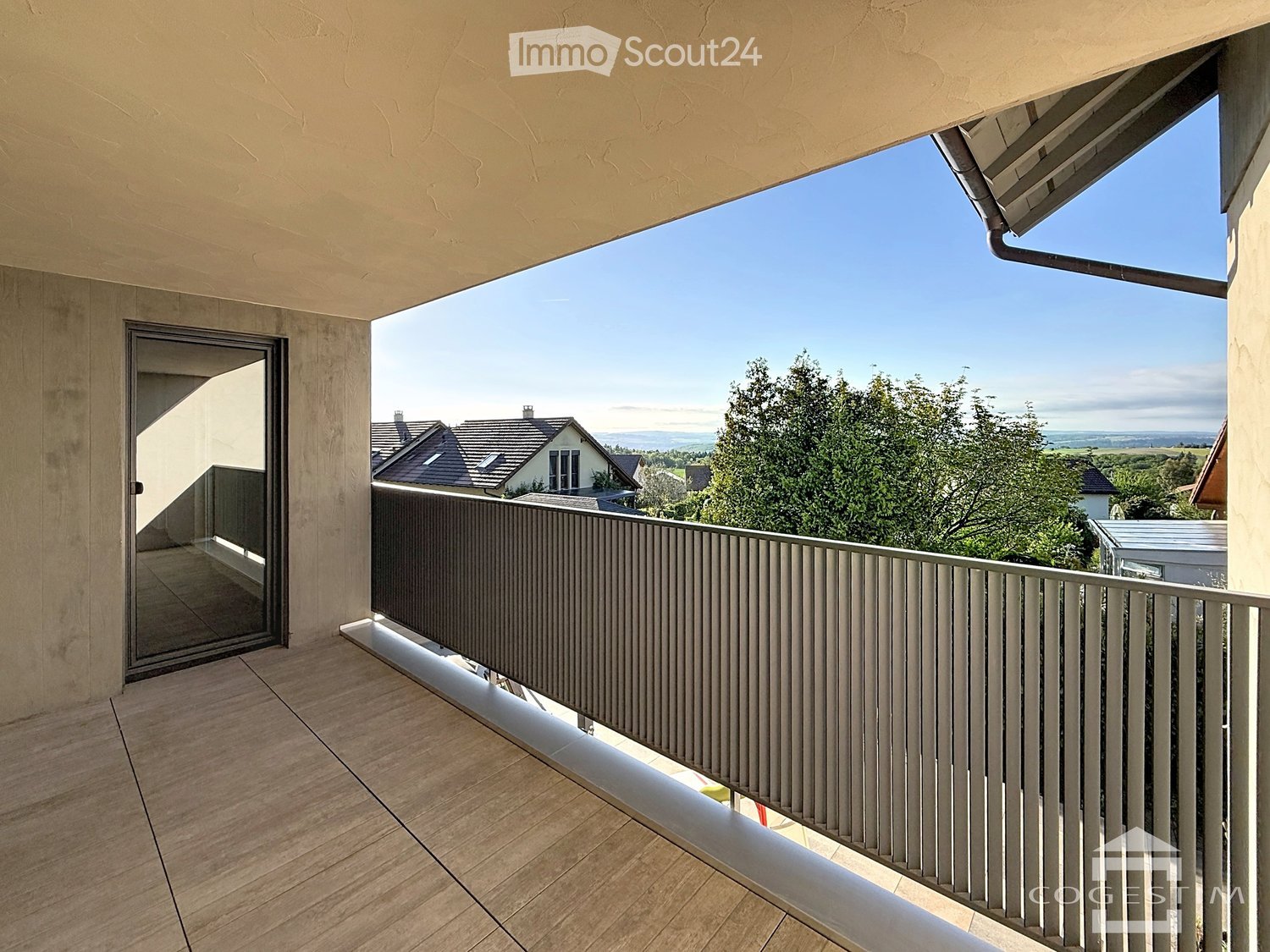 Balcony with wooden flooring, metal railing, and a view of the surrounding landscape and houses.