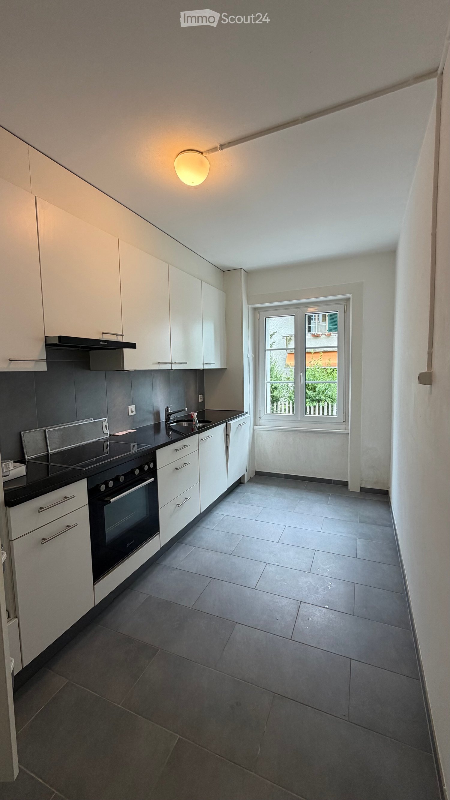 Modern kitchen with white cabinets, black countertops, and stainless steel appliances, including an oven and range hood. The space features a large window with a view of greenery outside.