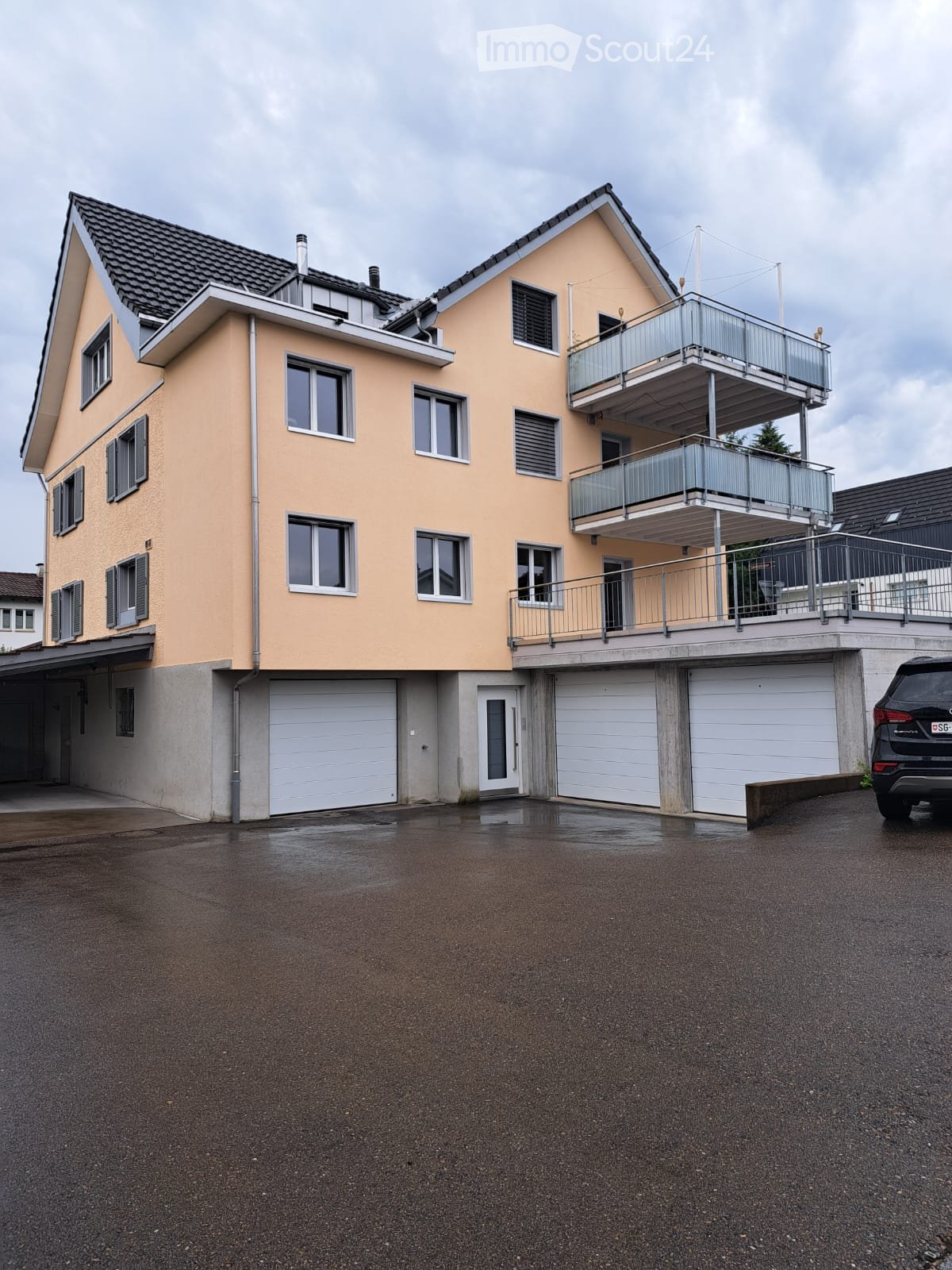 Two-story house with beige exterior, multiple windows, garage, and balcony on the upper level.