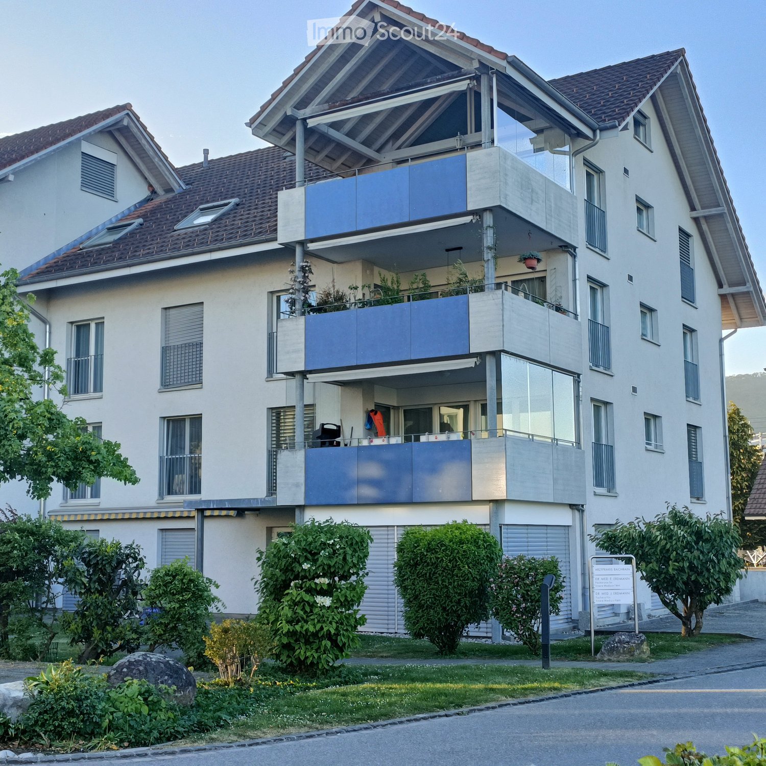 Modern two-story house with multiple balconies, large windows, and a well-maintained garden.