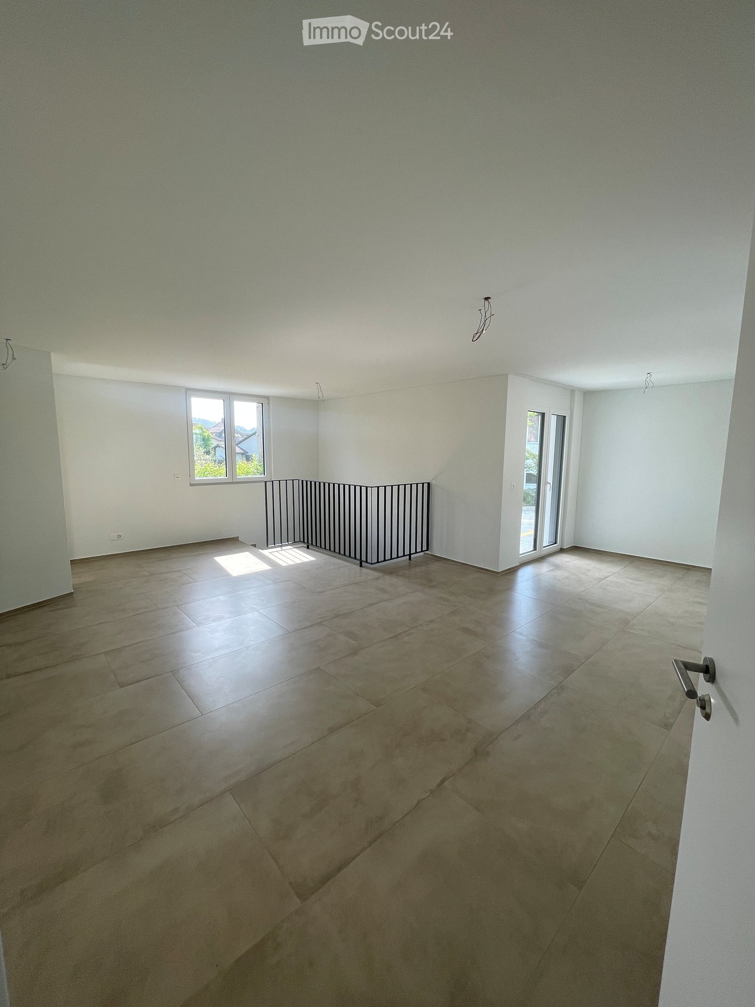 Empty room with tiled floor, white walls, and large windows, featuring a metal safety barrier near the window.