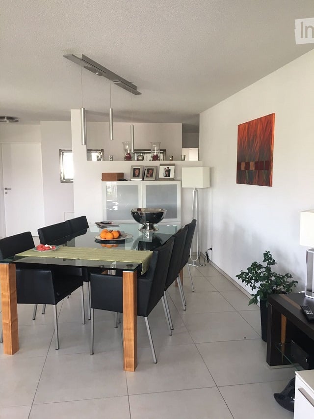 Modern dining area with a glass dining table, black chairs, a floor lamp, a cabinet, and artwork on the wall.