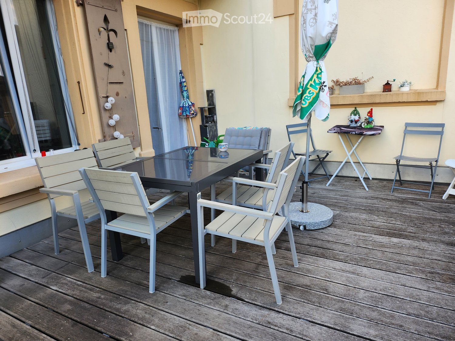 Balcony with wooden decking, glass table, several chairs, and an umbrella.