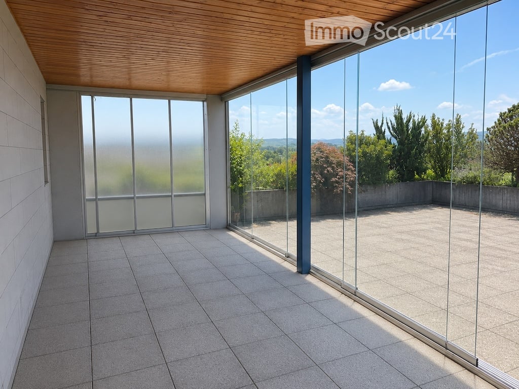 Modern balcony with large glass walls, tiled floor, wooden ceiling, and scenic mountain view.