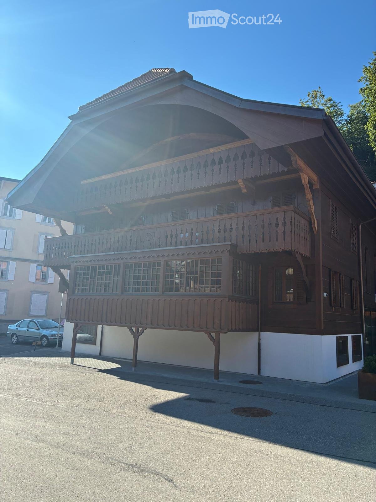 A two-story wooden house with ornate balconies and decorative railings, featuring multiple windows and a sloped roof.
