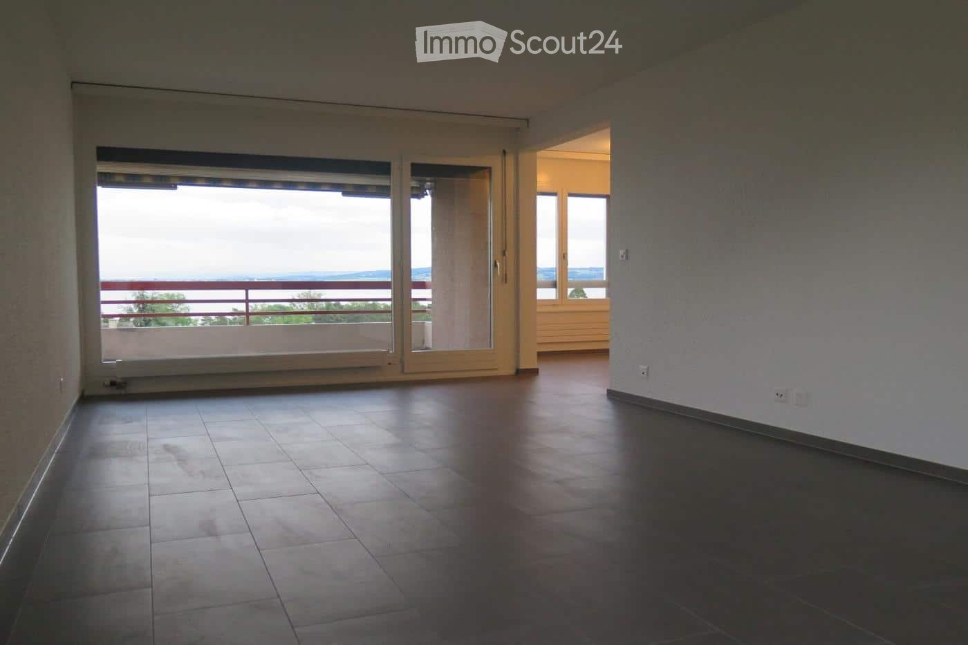 Empty room with tiled floor, large sliding glass doors leading to a balcony with a scenic view, and white walls.