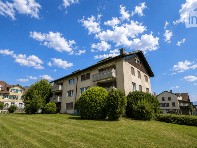 A multi-story residential building with balconies, surrounded by well-maintained green lawns and trees.