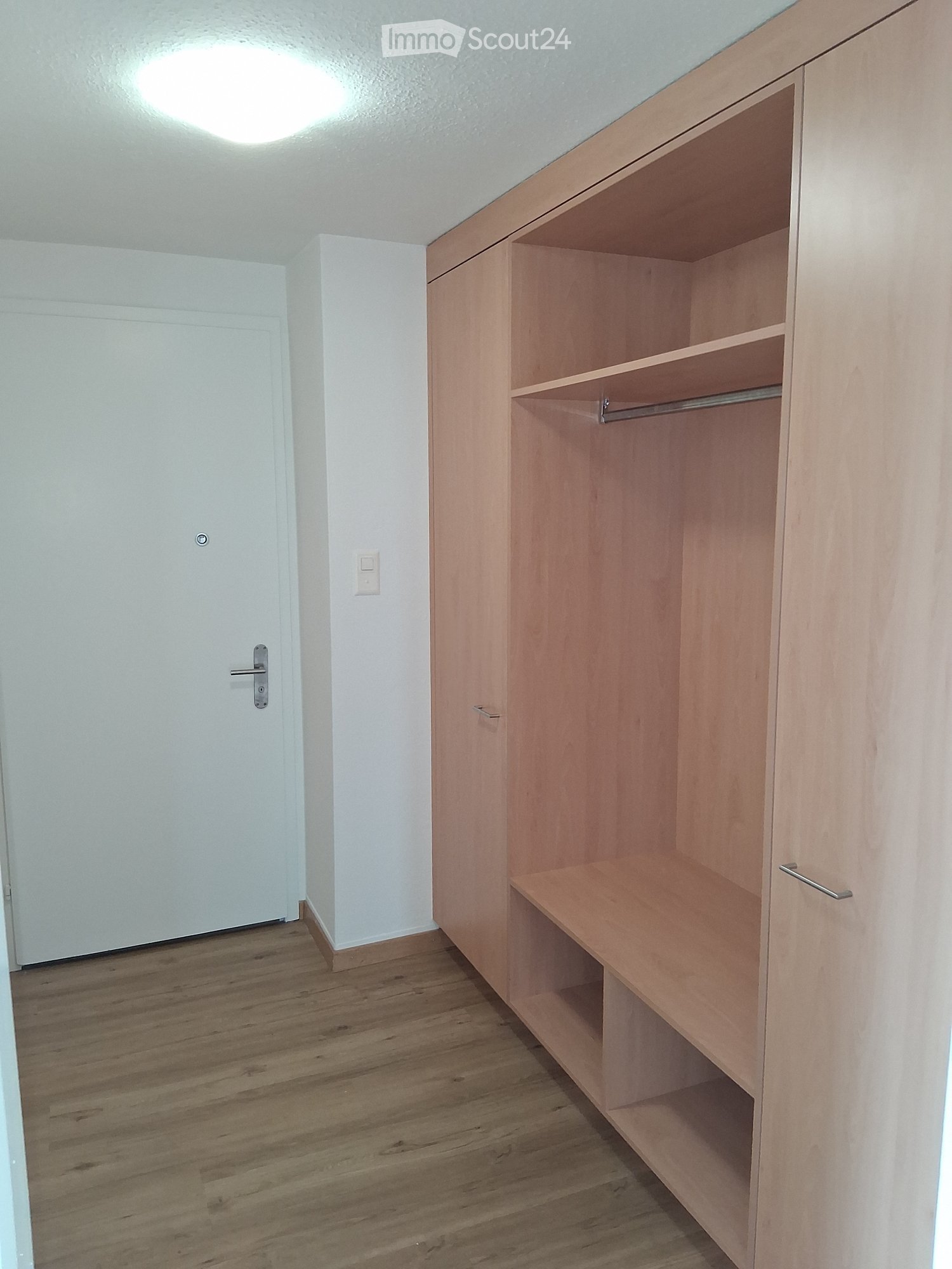 Empty room with wooden floor, white walls, and built-in wooden closet with shelves and hanging rod.
