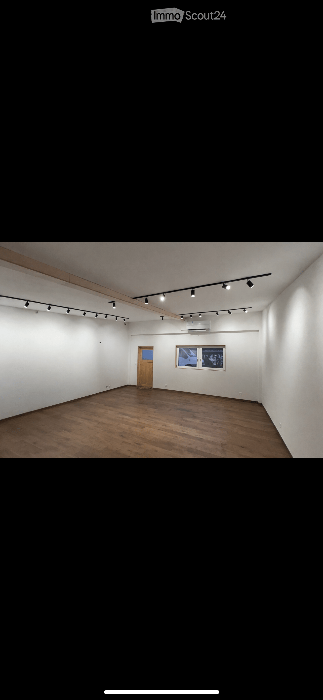 Empty room with wooden flooring, white walls, a single door, and a window with a view of a vehicle outside. Track lighting is mounted on the ceiling.
