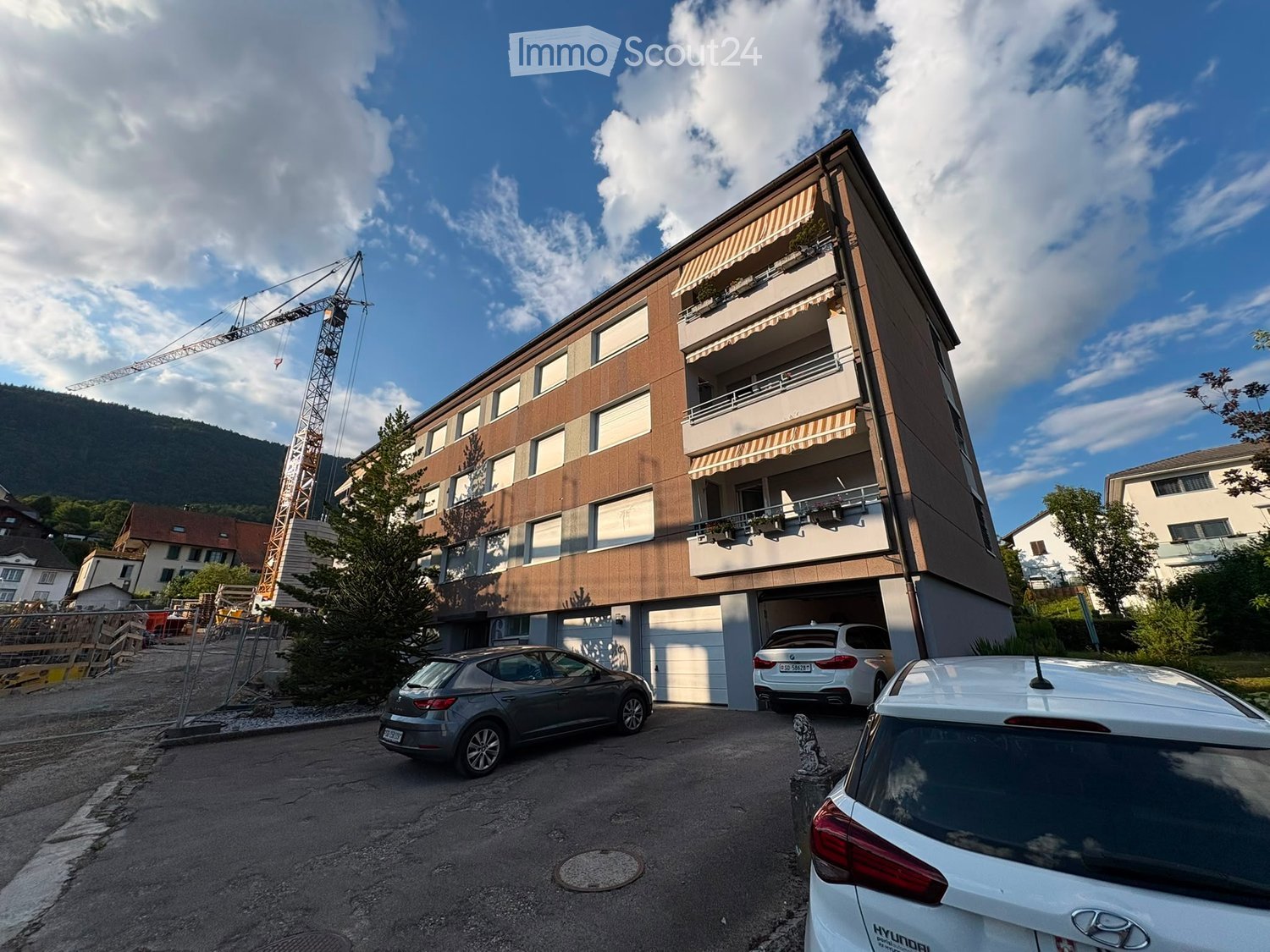 Modern multi-story building with balconies, garage, and several parked cars in front.