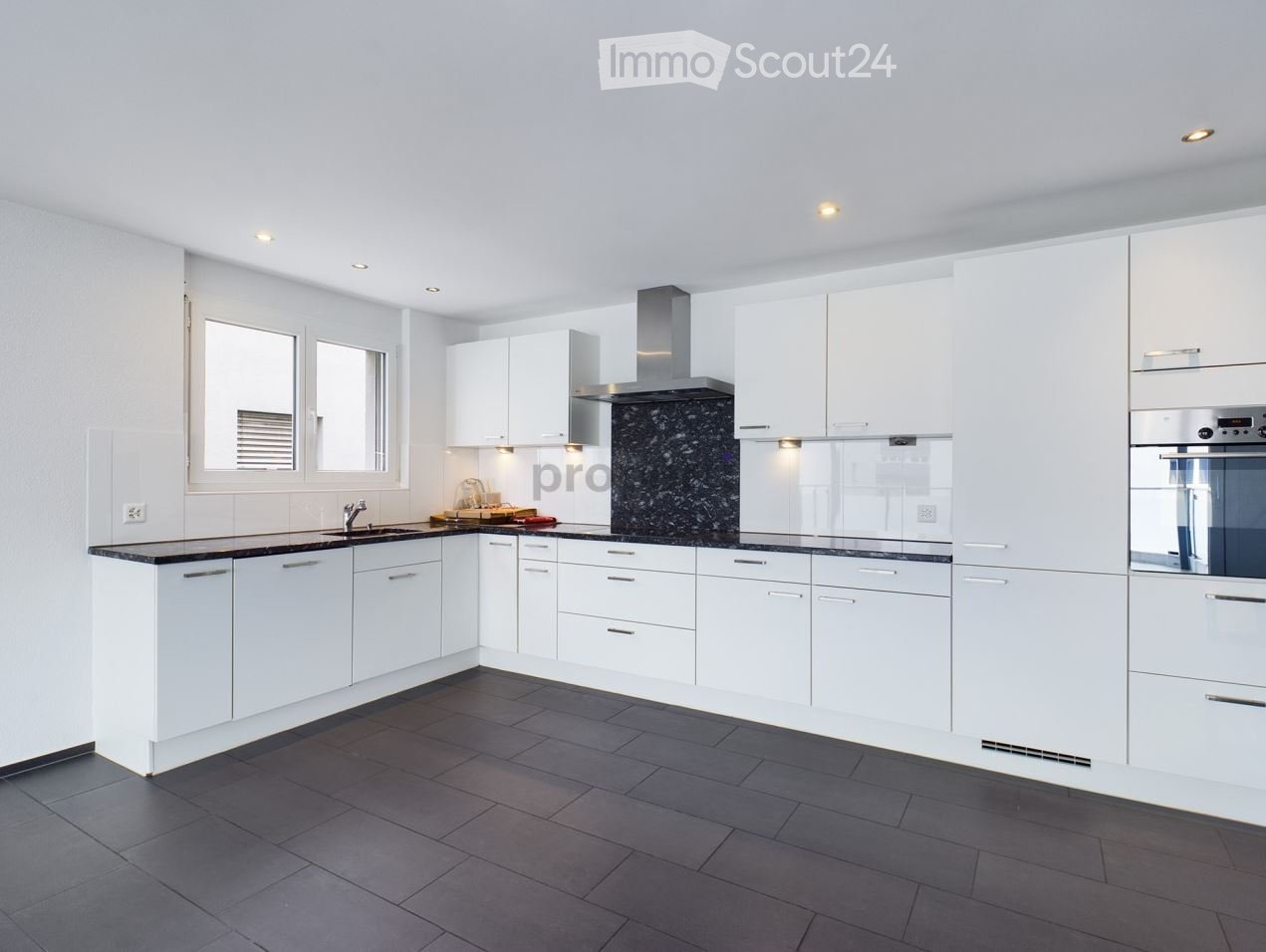 Modern kitchen with white cabinets, dark countertops, and stainless steel appliances. Features a sink, faucet, oven, and range hood.