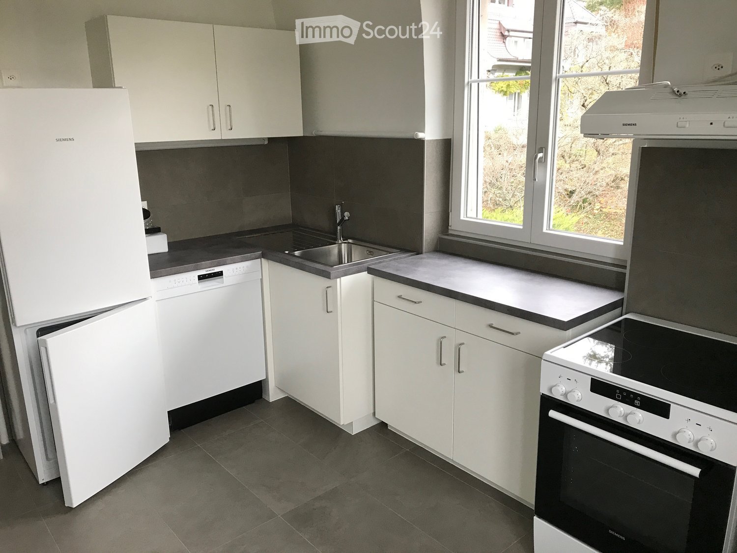 modern kitchen, white cabinets, gray tiled floor, stainless steel sink, refrigerator, dishwasher, stove, window