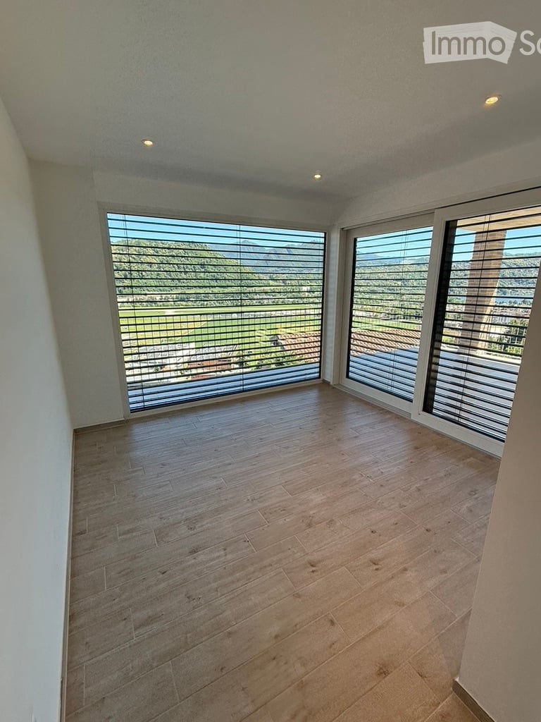Empty room with wooden flooring, large windows with blinds, and a scenic view of the landscape.