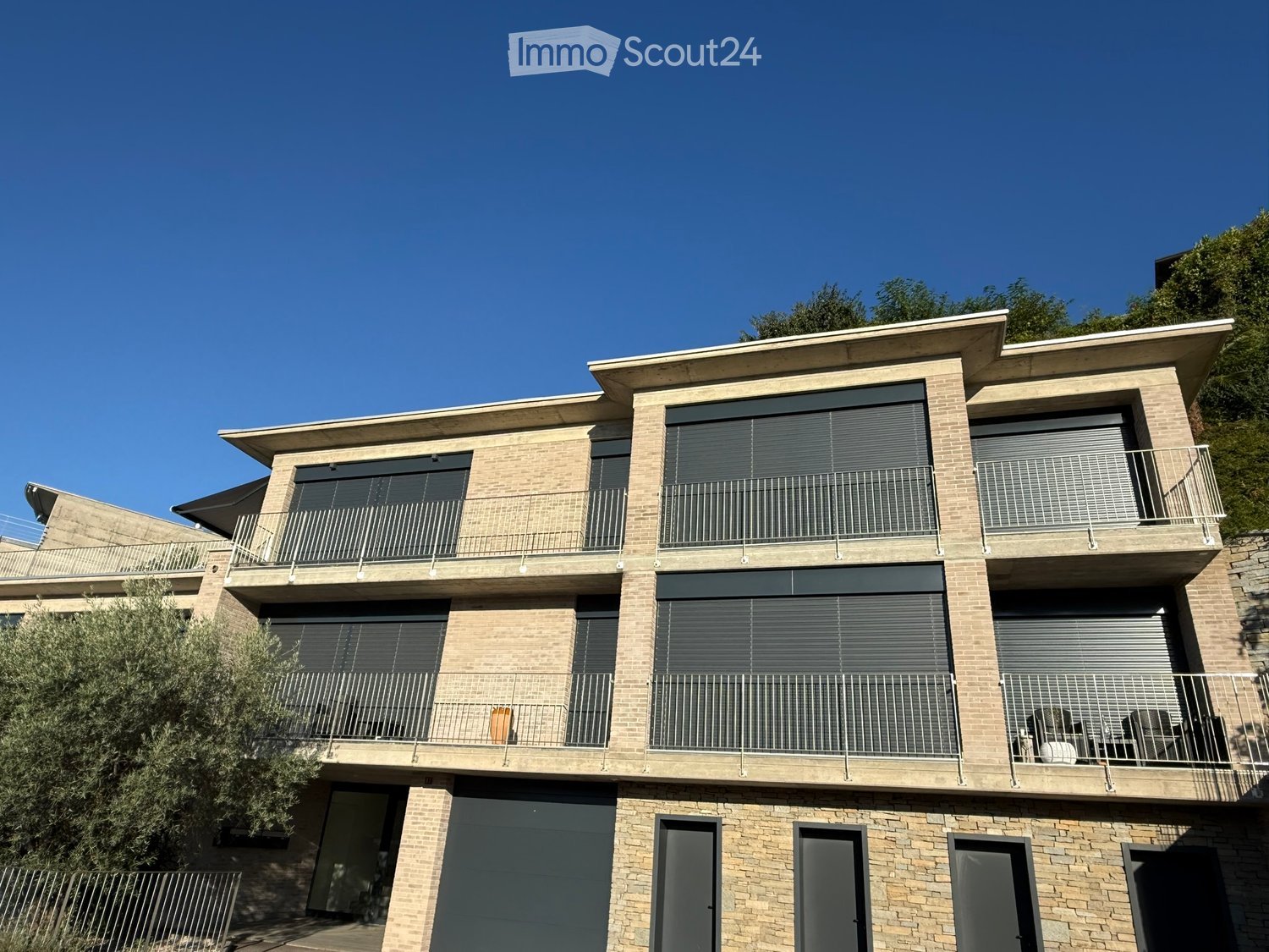 Modern two-story house with brick facade, large windows, balconies, and a garage entrance.