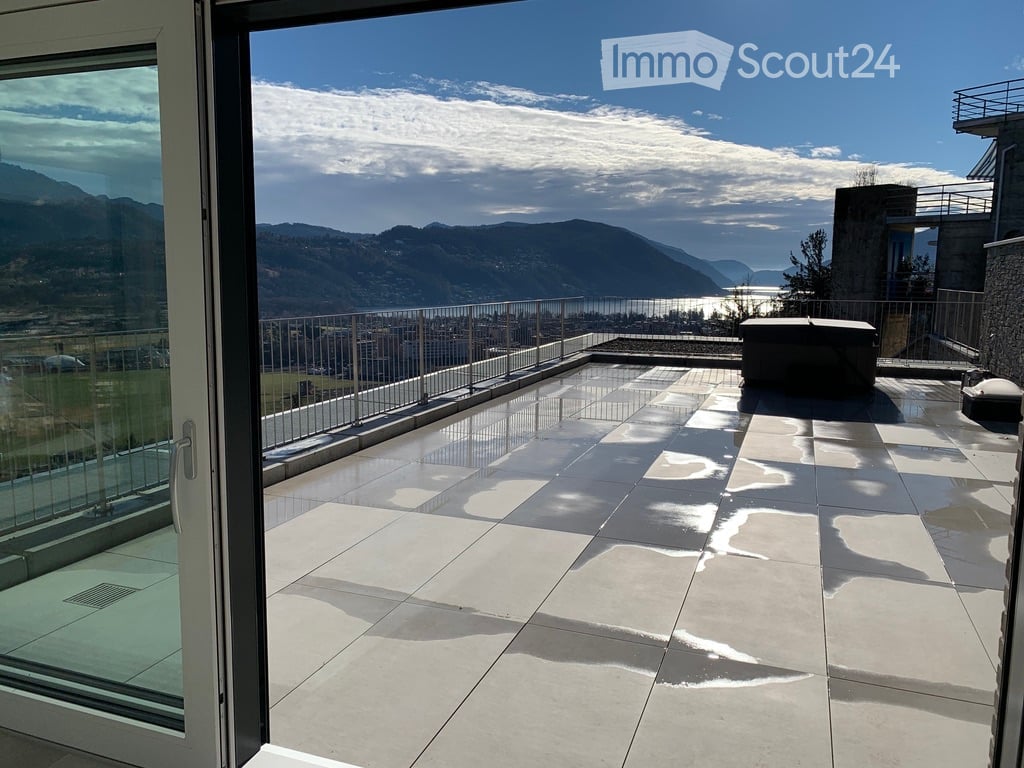 Modern balcony with large glass doors, tiled floor, metal railing, and scenic mountain and lake view.