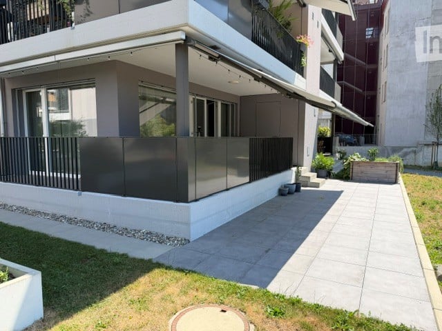 Modern two-story building with a covered balcony area, large windows, and a small garden space.
