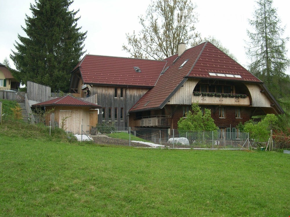 Two-story house with red tile roof, wooden facade, and balcony. Includes a small garage and fenced yard.