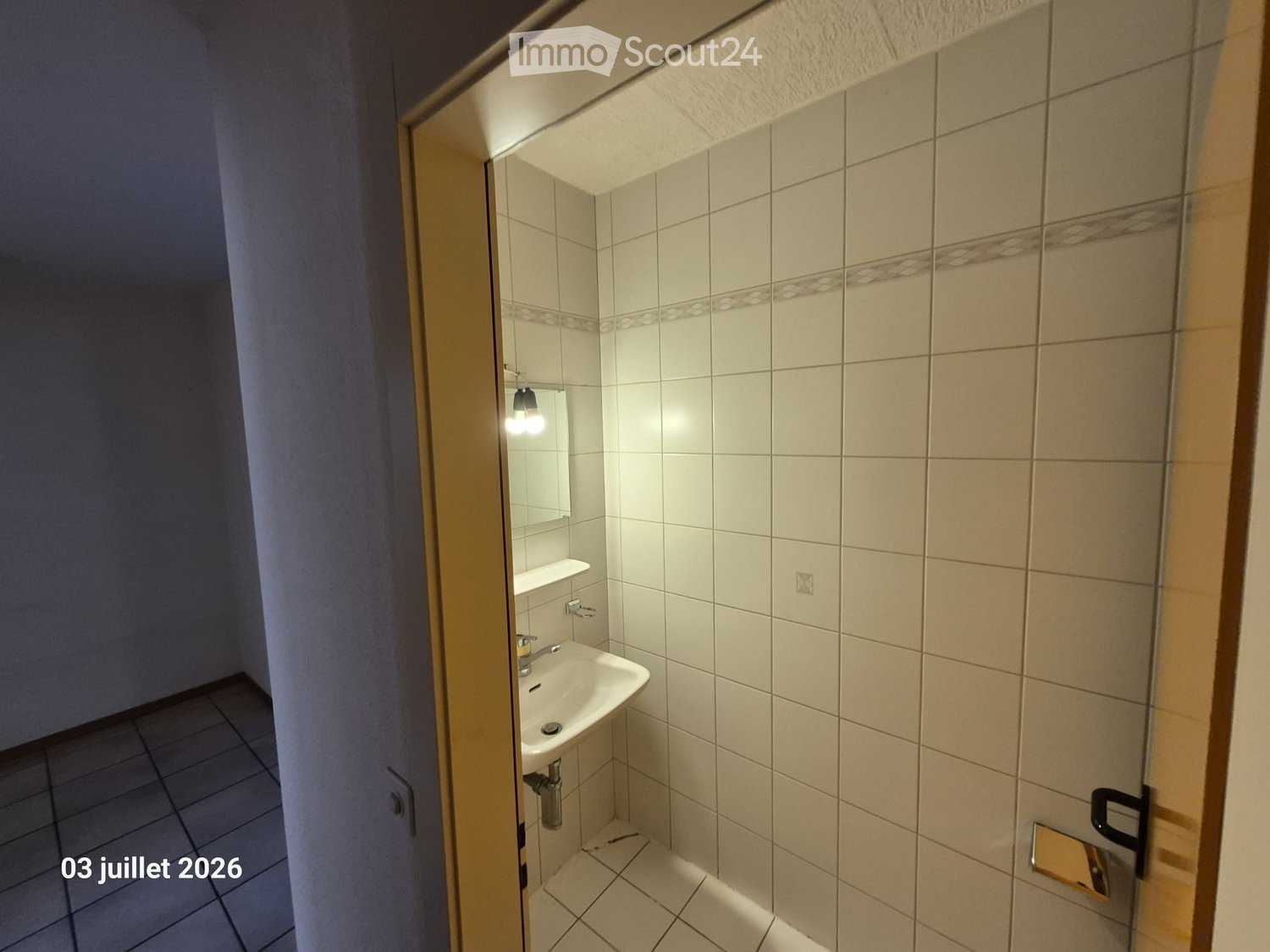 Small bathroom with white tiled walls and floor, a white sink, a mirror, and a light fixture above the sink.