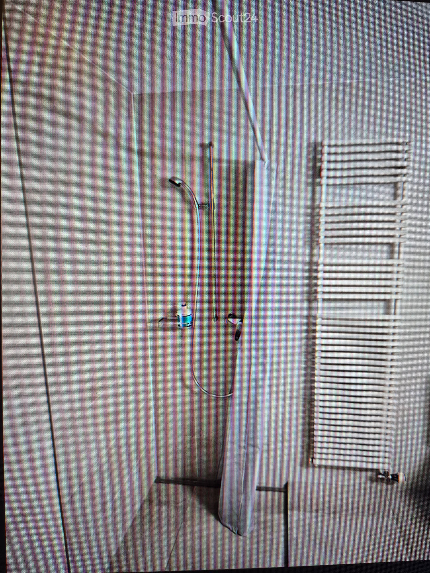 Modern shower area with a sleek, grey tiled wall, a white radiator, and a small bottle on the wall.