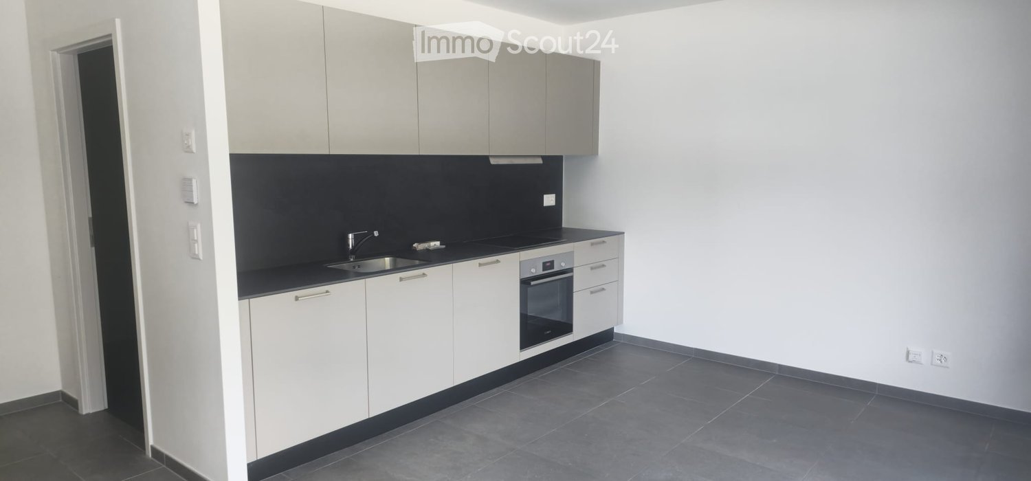 Modern kitchen with white cabinets, black countertops, stainless steel sink, and built-in oven. The space is clean and well-lit with grey tiled flooring.