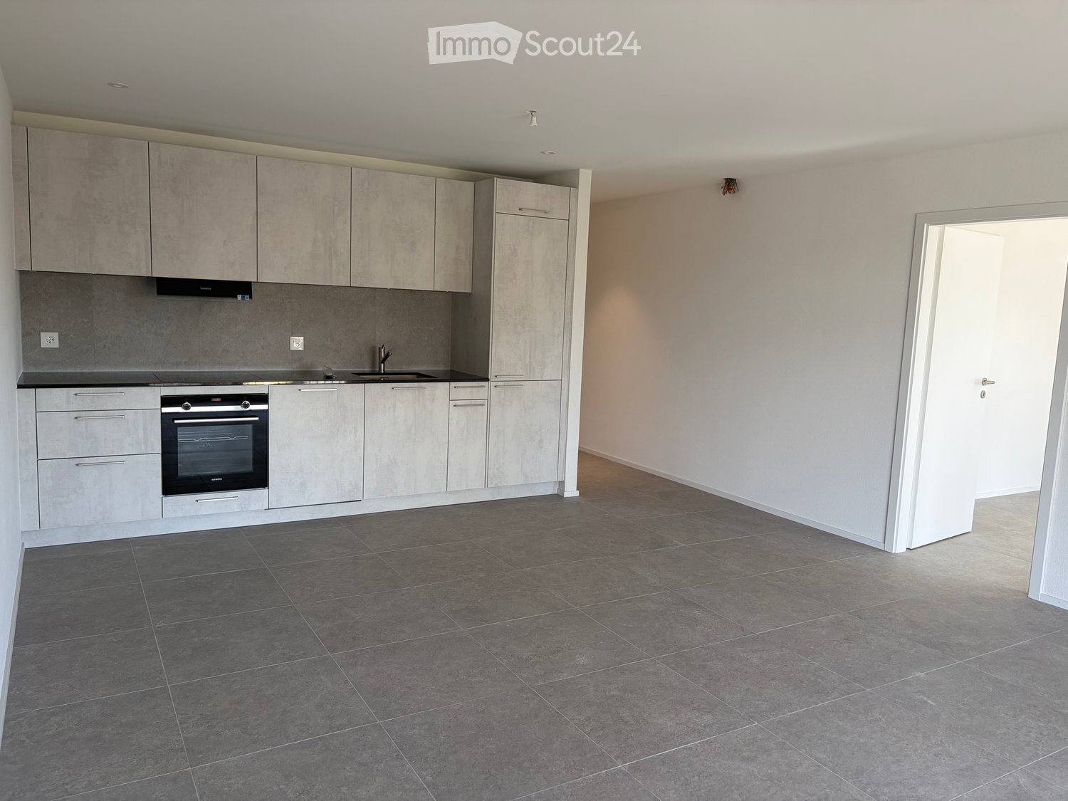 Modern kitchen with grey tiled floor, grey cabinets, and stainless steel appliances including an oven and sink.