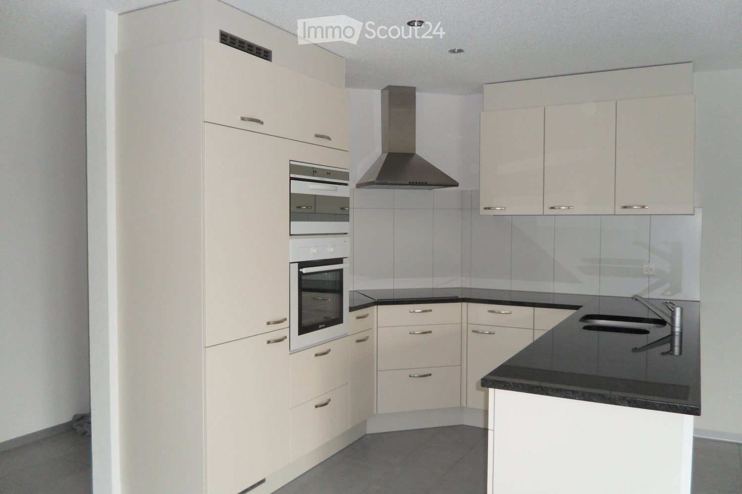 Modern kitchen with light-colored cabinets, stainless steel appliances, black countertops, and a built-in oven.