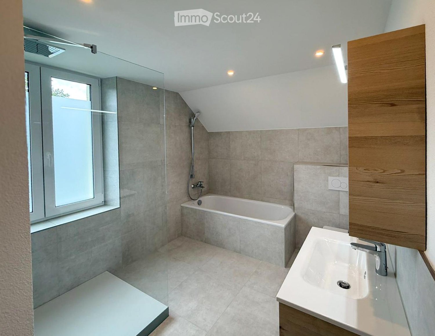 Modern bathroom with a bathtub, sink, and glass-enclosed shower area. Features include a window, wooden cabinet, and sleek fixtures.