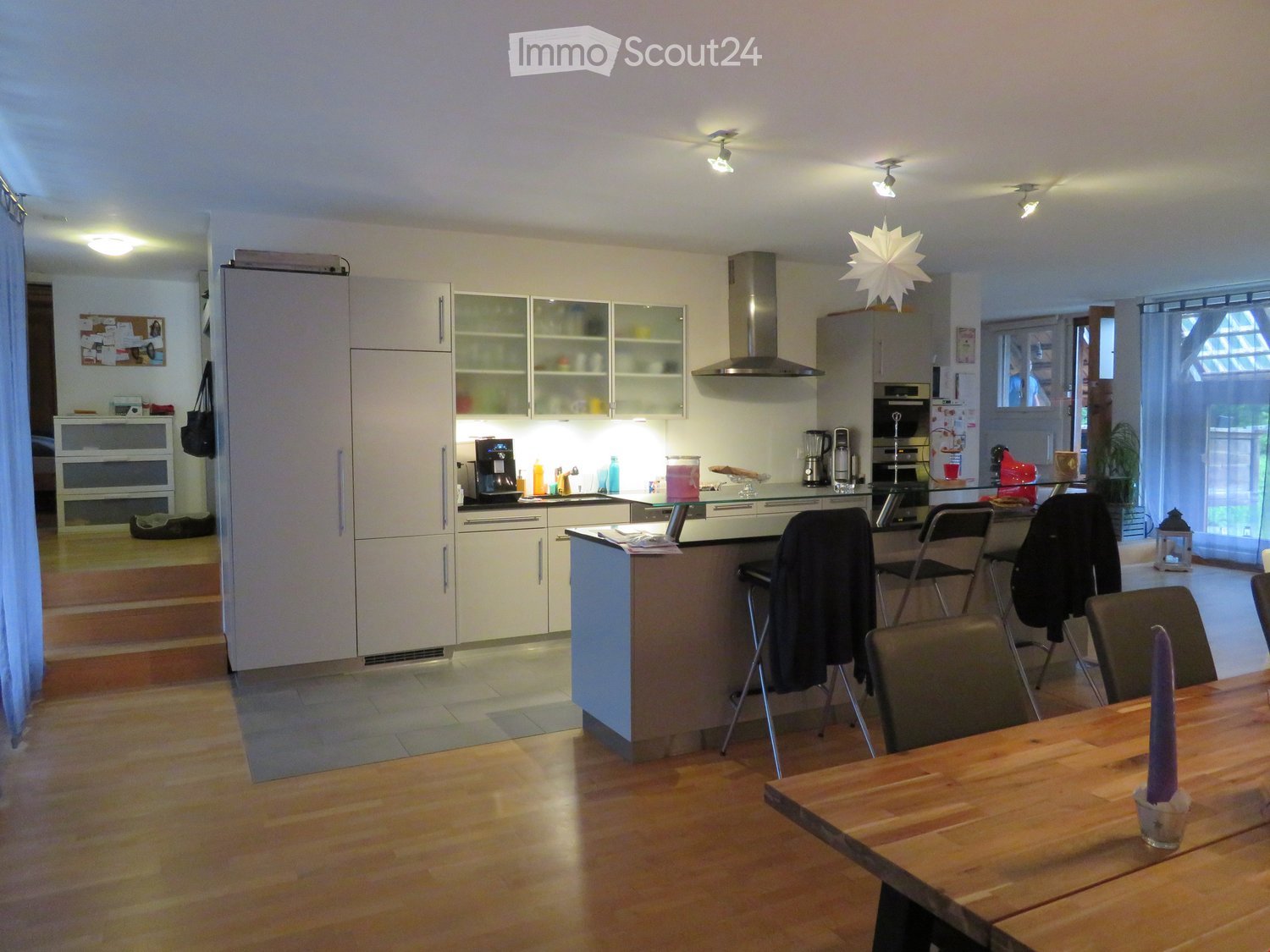 Modern kitchen with white cabinets, stainless steel appliances, island, and dining area with wooden table and chairs.