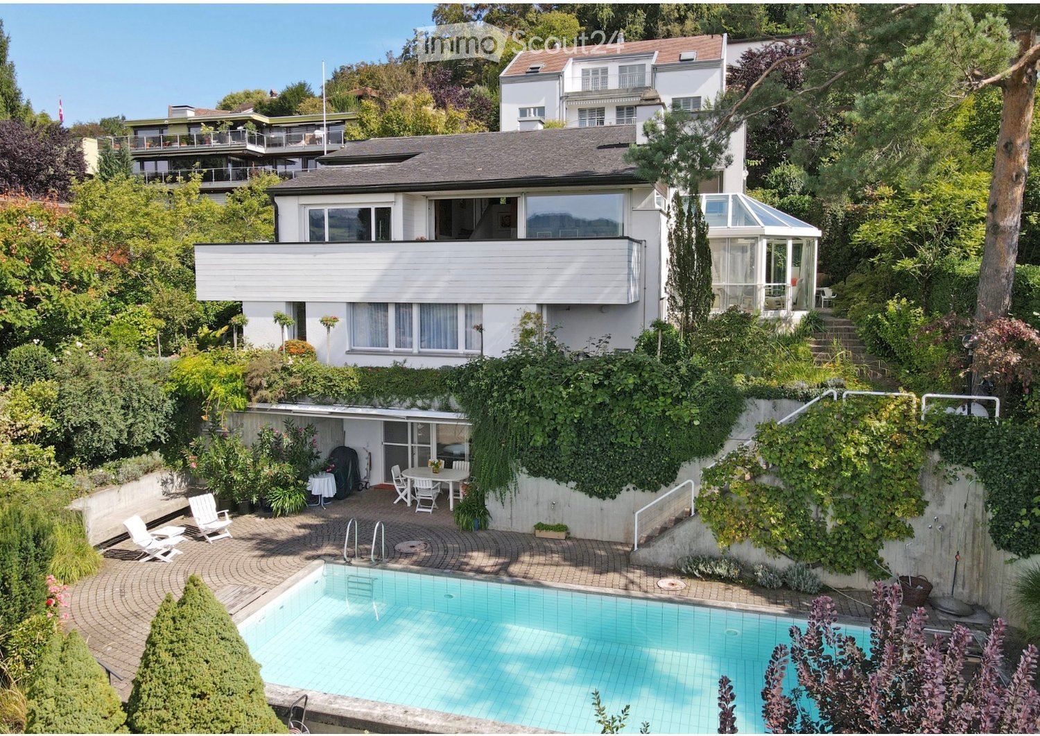 House. A multi-story house with a modern design, surrounded by lush greenery. Features include a swimming pool, outdoor seating area, and a covered patio with a glass roof.