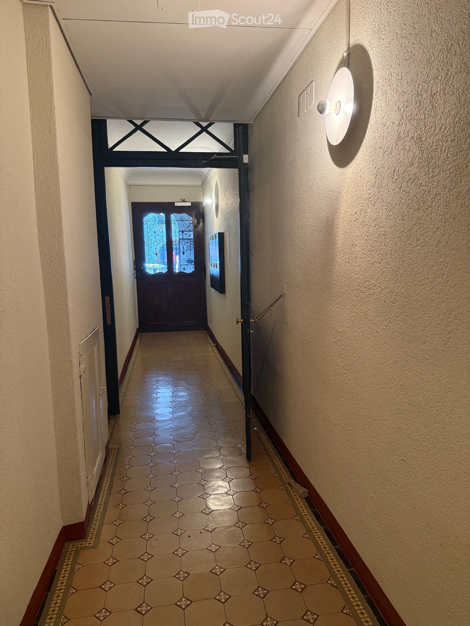 Hallway with beige tiled floor, light-colored walls, and a decorative door at the end.