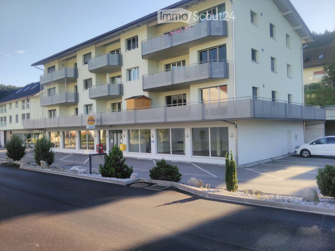 4-story apartment building, balconies, 2 cars parked, garden in front